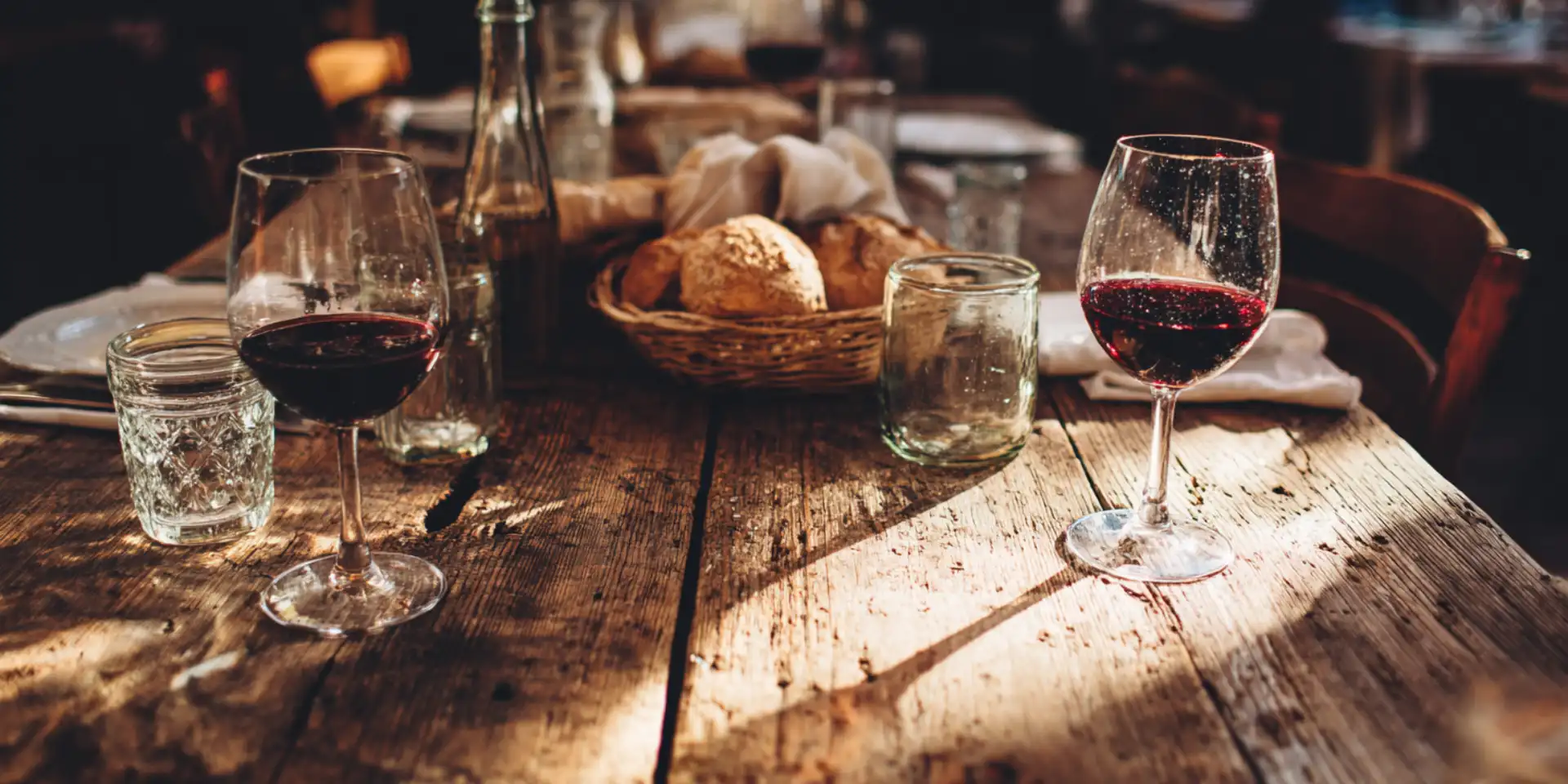 Italian lunch table with worn wood, mismatched wine glasses, and bread basket in natural afternoon light
