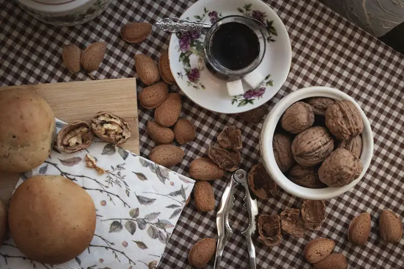 A cozy breakfast setup with nuts, buns, and coffee on a checkered tablecloth.