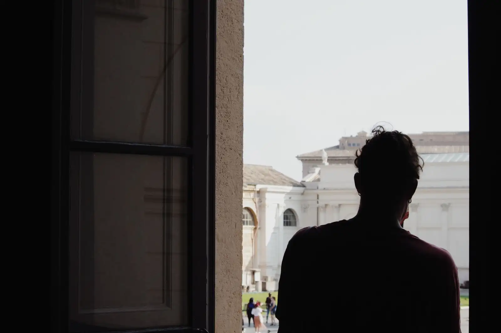 A silhouette of a man stands in a doorway, viewing historic Roman architecture under daylight.