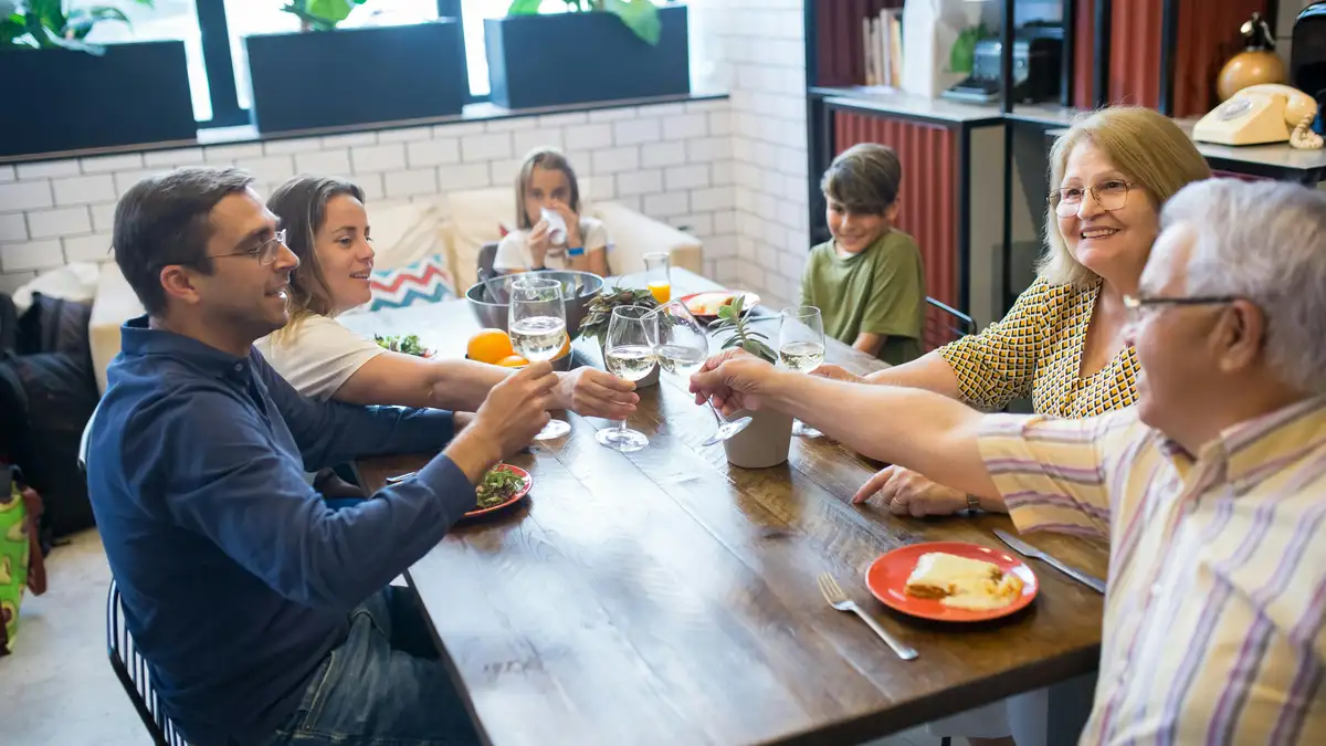 Joyful Italian family toasting with red wine glasses around a candlelit table, savoring pasta and bread in a warm indoor gathering.
