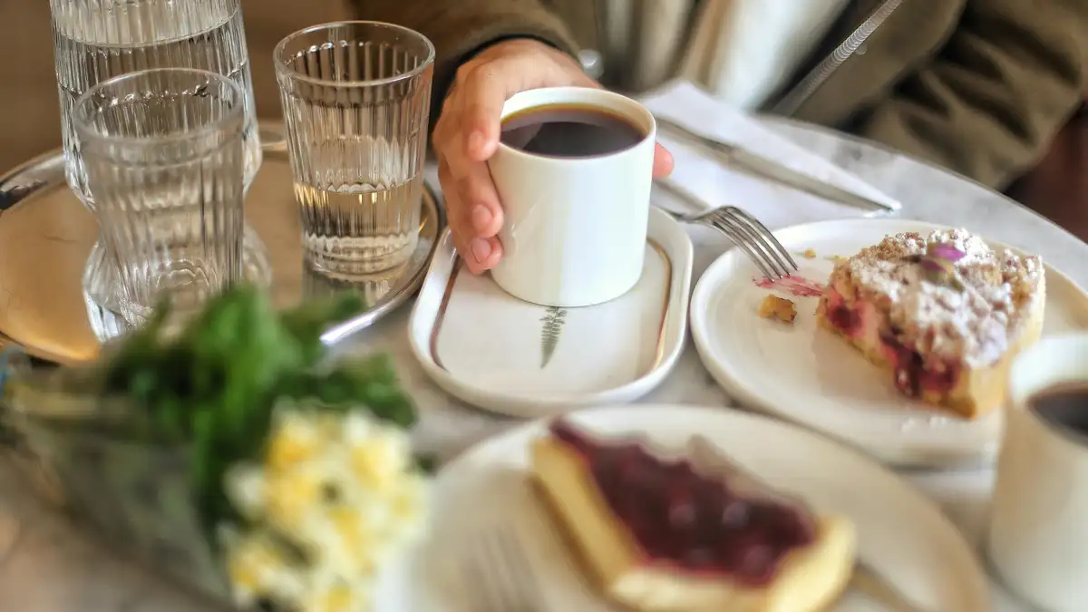 Warm steaming cup of coffee beside cinnamon buns and berry cakes on rustic table in cozy Swedish fika cafe.