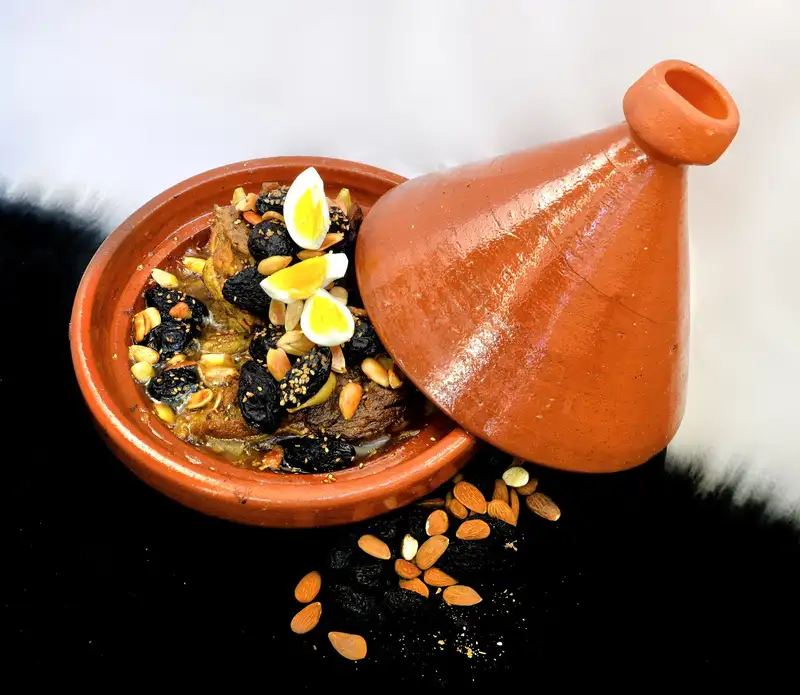 Delicious Moroccan lamb tagine with almonds, prunes, and quail eggs in a clay pot.