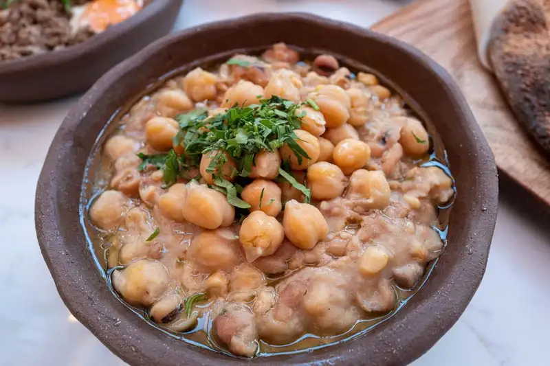 Close-up of a hearty chickpea stew garnished with fresh herbs, served in a rustic brown bowl.