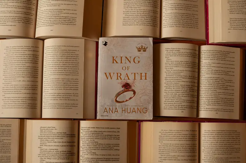 Centered book 'King of Wrath' by Ana Huang amidst open books.